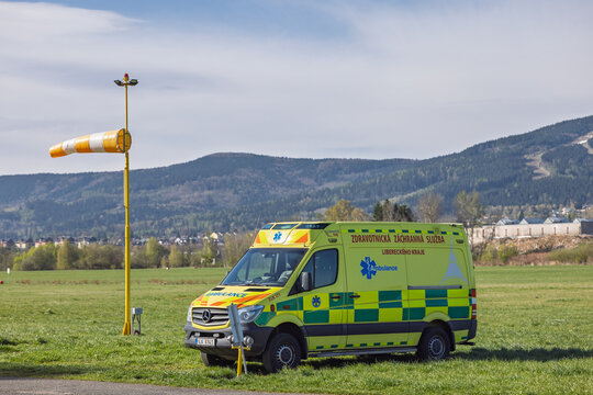 Emergency Ambulance Parked On Airfield Next To Windsock With Mountain Landscape Background. Liberec City, Czech Republic