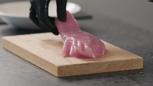 Slow motion man hands in black gloves slicing turkey fillet on oak wood board