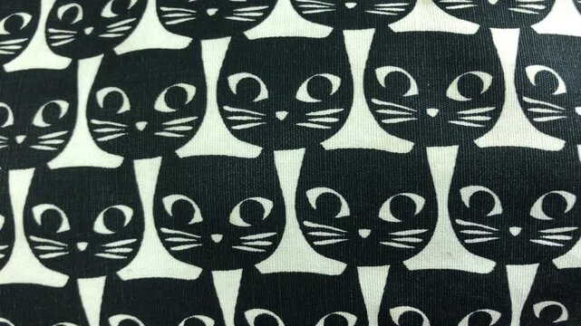A close-up view of a repeating pattern of black cat faces with white eyes and whiskers on a white background.