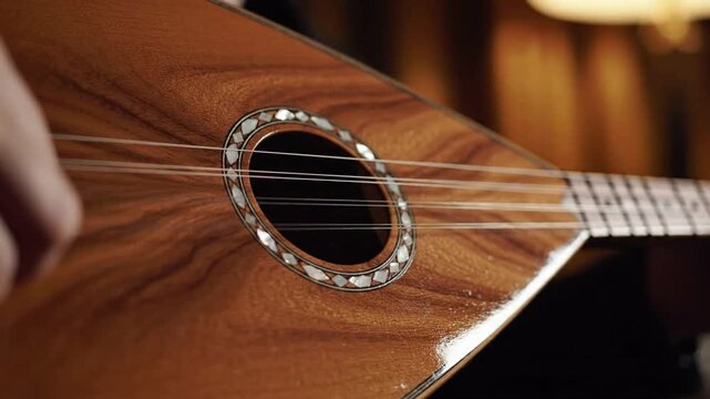Close-up detail of a person playing a wooden stringed instrument with intricate mother-of-pearl inlay around the soundhole, warm lighting