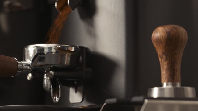 Slow motion freshly ground coffee falls into portafilter from grinder closeup
