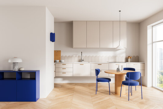 Bright minimalist kitchen interior with beige cabinets, blue accents, wooden dining set and large window in modern apartment. 3D Rendering