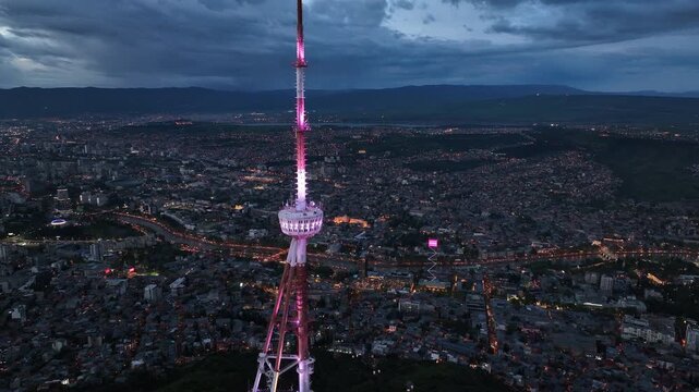 Aerial view of the Funicular Restaurant at Mtatsminda Park during sunset. Dynamic drone shot of a TV tower with Tbilisi city in the background.