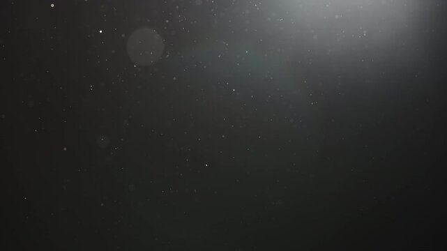 Slow motion real dust particles floating mid air over dark background