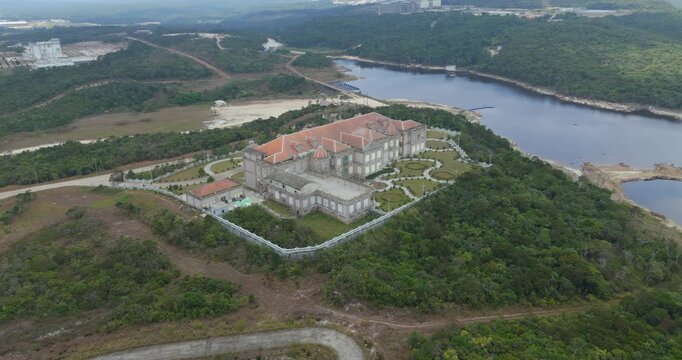 backward aerial view of a grand red roofed mansion with manicured gardens on Bokor Mountain, Cambodia, surrounded by lush forest near Bokor Lake.