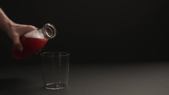 Slow motion man hand pour berry drink into tumbler glass on black paper background with copy space
