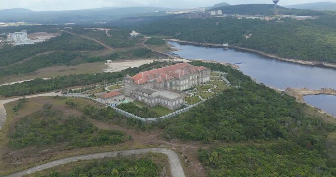 backward aerial view of a grand red-roofed mansion with manicured gardens on Bokor Mountain, Cambodia, surrounded by lush forest near Bokor Lake.