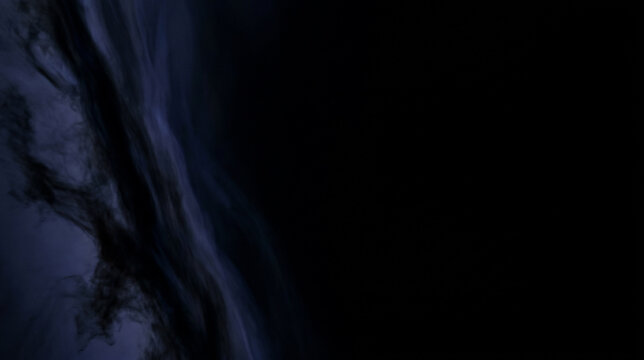 Opaque deep indigo interstellar gas filaments and swirling charcoal dust clouds concentrated on the far left of a black studio background with copy space void