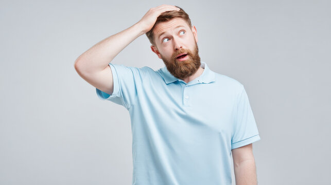 Surprised young man in blue shirt touching head in a moment of realization against gray background