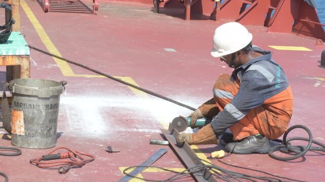 crew member using electric angle grinder to cut steel material on the deck of a cargo vessel during ship maintenance and repair operation at sea