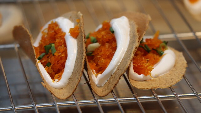 Close-up of traditional Thai crispy crepes (Khanom Buang) filled with white cream, savory orange coconut, and green onions on a cooling rack.