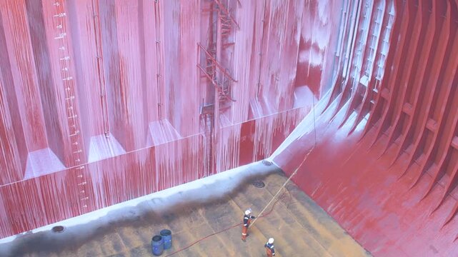 high angle view of seafarers spraying and applying cleaning chemical on cargo hold interior surfaces of a bulk carrier vessel during hold preparation and maintenance operations