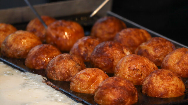 Rows of golden brown Takoyaki octopus balls being flipped and cooked in a specialized takoyaki pan at a street food market stall