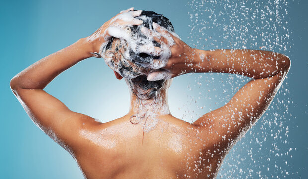 Hair care, splash and back of woman in studio for shower with grooming, hygiene or wellness with soap. Beauty, water and person with clarifying shampoo, conditioner or treatment by blue background.