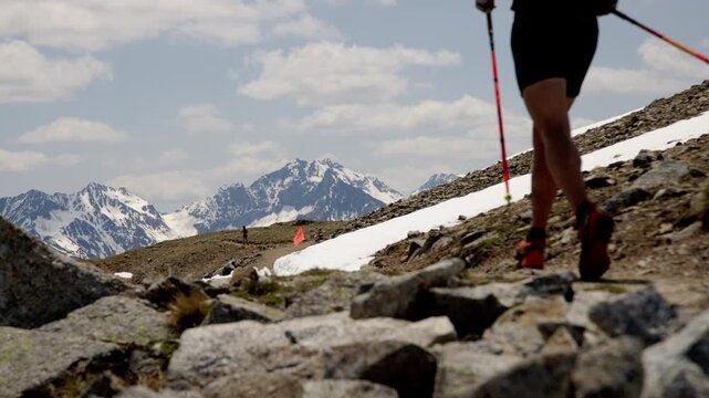 A Runner With Trekking Poles is Approaching a Red Flag Along the Rugged Alpine Trail During the Livigno Sky Marathon in Livigno, Italy - Medium Shot