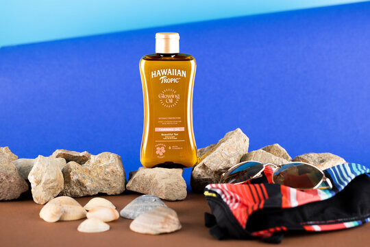 Hawaiian Tropic Glowing Oil tanning oil presented in a tropical summer-inspired product photography scene with seashells, sunglasses and beachwear emphasizing vacation, tanning and skincare lifestyle 