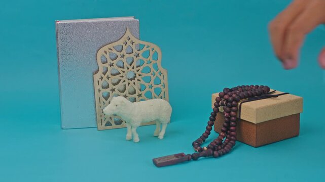 Festive Eid al-Adha flatlay featuring sheep figurine, silver book, and tasbih on turquoise backdrop