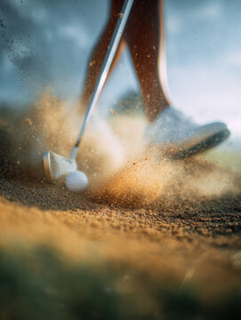 Golfer striking a ball out of a sand trap with a golf club on a golf course in dramatic action with flying sand and soft sunlight background