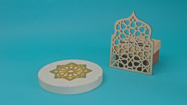 Toy sheep stands beside an Islamic geometric ornament and laser-cut mosque on blue background