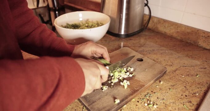 Person chopping fresh spring onions on a wooden cutting board