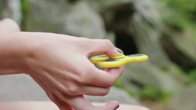 Close up of female hand spinning yellow fidget spinner toy outdoors.