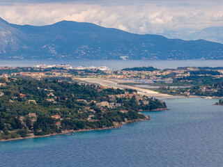 Fototapeta premium Panoramic High Angle View of Corfu International Airport Runway and Port with Large Cruise Ships in the Distance - Scenic Mediterranean Island Landscape with Mountains and Ionian Sea in Greece