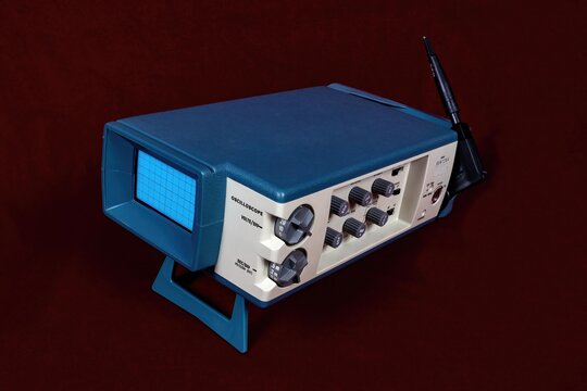 Vintage portable electronic field oscilloscope, blue and white, circa 1970s. Shown on red background. 
