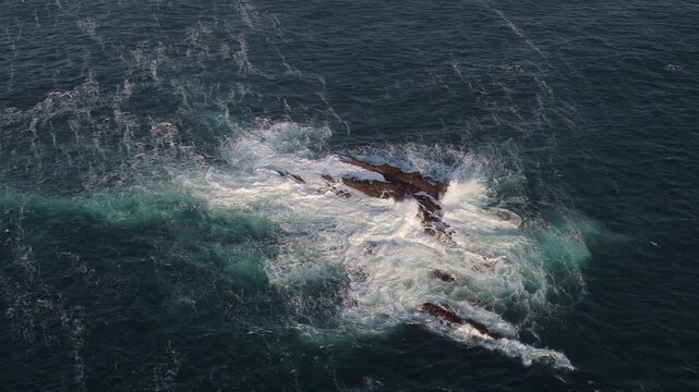 A dynamic aerial view of ocean waves in motion. Nature's raw power is evident in this seascape. Turbulent ocean waters surround a rocky outcrop.