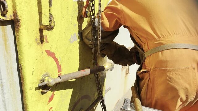 ship fitter make repair by welding water tight door at open deck. weld spatter. chain block 