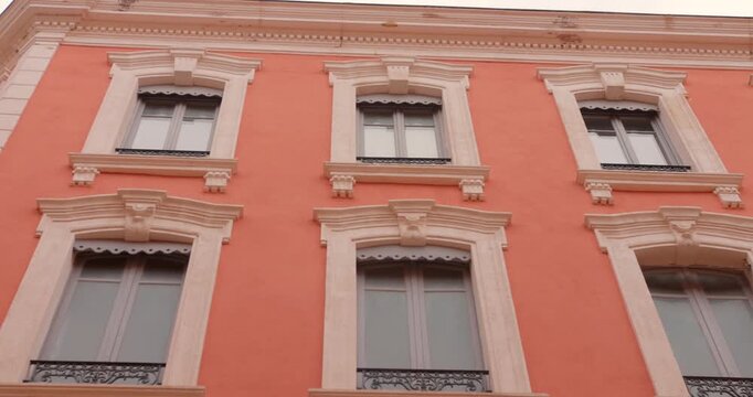 Camera tilts up along a vibrant orange neoclassical building facade with decorative stone window frames in the old town of Narbonne, southern France.