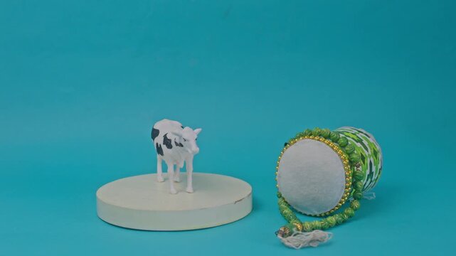 Hand places cow figurine on pedestal next to bedug drum and prayer beads for Eid al-Adha