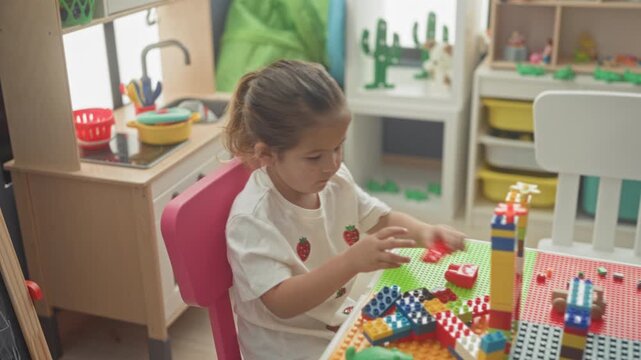 Hispanic girl stacking colorful toy blocks with hand, constructing a tower in a building; concentration learning creativity.
