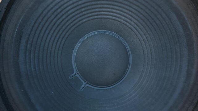 Macro view of a dark paper subwoofer cone vibrating intensely while playing low frequency bass music. Concept of high volume acoustic sound waves and powerful audio systems.