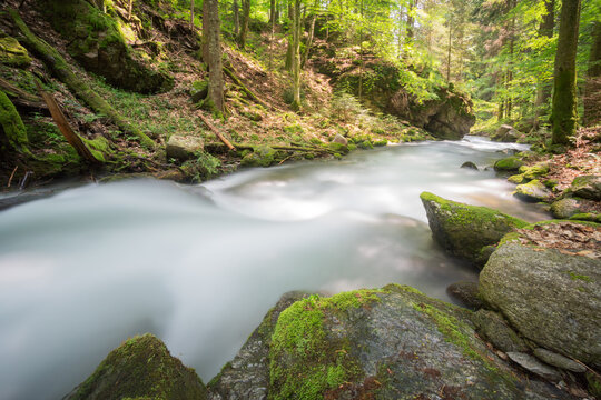 View of Vajskovska dolina with a silky mountain stream flowing over mossy rocks through a lush green forest with sunlight in Dolna Lehota, Banskobystricky kraj, Slovakia.