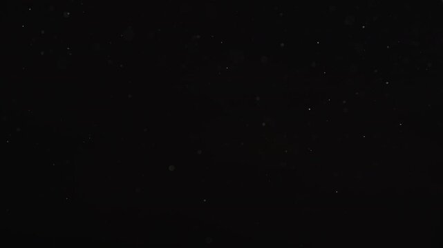 Slow motion real dust particles floating mid air over dark background