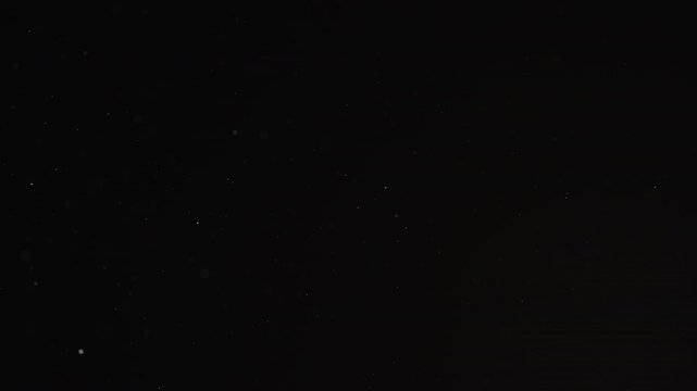 Slow motion real dust particles floating mid air over dark background