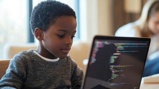A young boy intently focuses on a laptop displaying complex code.