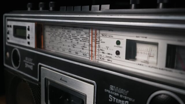 A detailed close-up shot of an analog radio frequency dial on a classic, vintage boombox. The display shows various radio bands and city names, evoking a nostalgic and retro feeling.