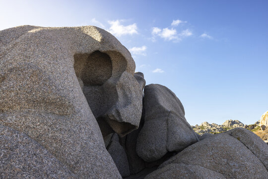 View of unique granite rock formations with hollowed-out shapes under a clear blue sky at Capo Testa, Sardegna, Italy.