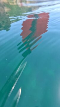 Water reflection ripples create an abstract pattern of distorted red and green colors on the surface of a calm turquoise sea during daytime