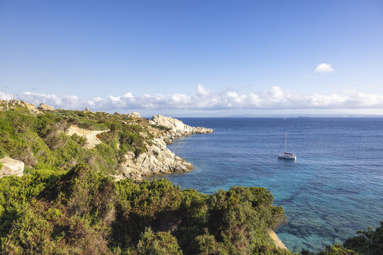 View of the rugged granite cliffs and turquoise waters with a sailboat anchored in the bay at Capo Testa, Sardegna, Italy.