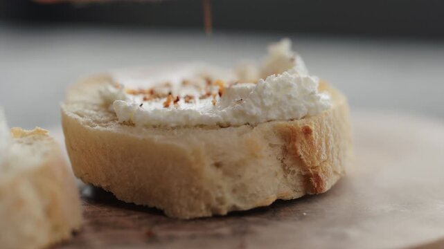 Slow motion spices fall on cream cheese on fresh baguette slice on olive board closeup