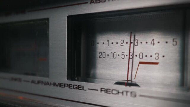Vintage analog audio recording level meter features striking red needles on a brushed metal plate. This classic hifi stereo equipment is captured with soft shallow depth of field.