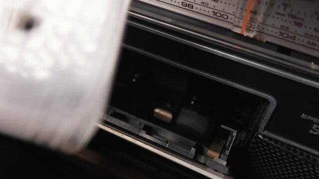 Vintage cassette tape player spins magnetic tape behind a brushed metal door in sharp macro detail. Concept of nostalgic analog media and retro authentic audio technology from past decades.