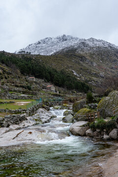 View of Praia Fluvial de Loriga with a cascading mountain stream, stone terraces, and snow-capped peaks under a cloudy sky Loriga, Distrito da Guarda, Portugal.