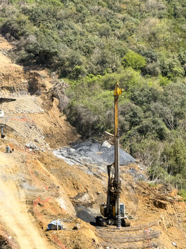 View of a large yellow drilling rig operating on a construction site with excavated earth and lush green forest in Sariyer, Istanbul, Turkey.