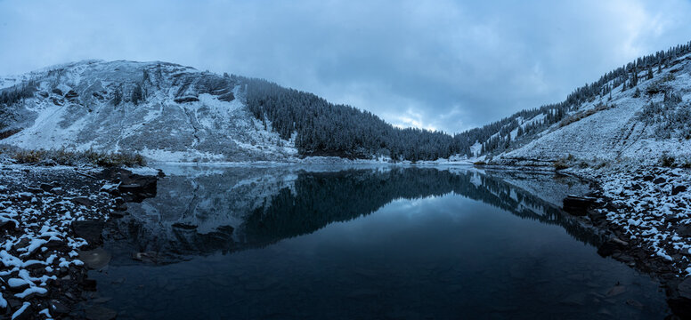 Panoramic view of Emerald Lake with snow-covered mountain slopes and dense pine forests reflected in the still water Larimer County, Colorado, United States.