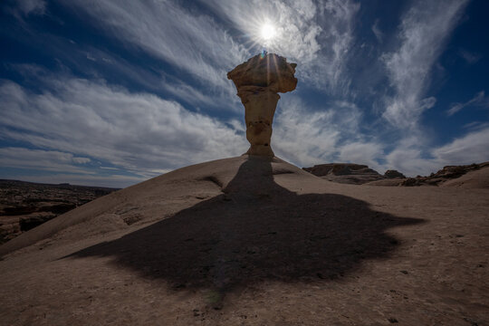 View of a unique sandstone hoodoo formation under a bright sun and wispy clouds in Moab, Utah, United States.