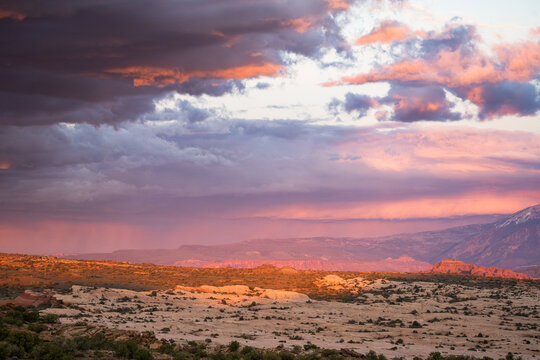 View of the desert landscape with red rock formations and dramatic sunset clouds over the horizon in Moab, Utah, United States.