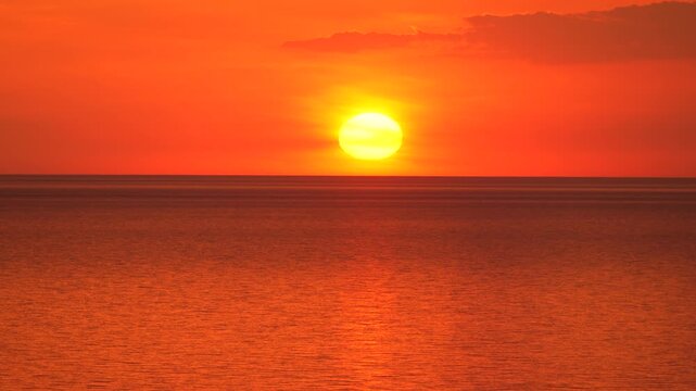 Sunset ocean horizon glowing sun setting over the calm sea under a dramatic red and orange sky